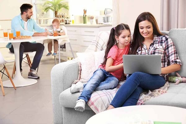 EVOAQ Home Ventilation image mother with daughter relaxing on couch on right looking at laptop father feeding baby son in background
